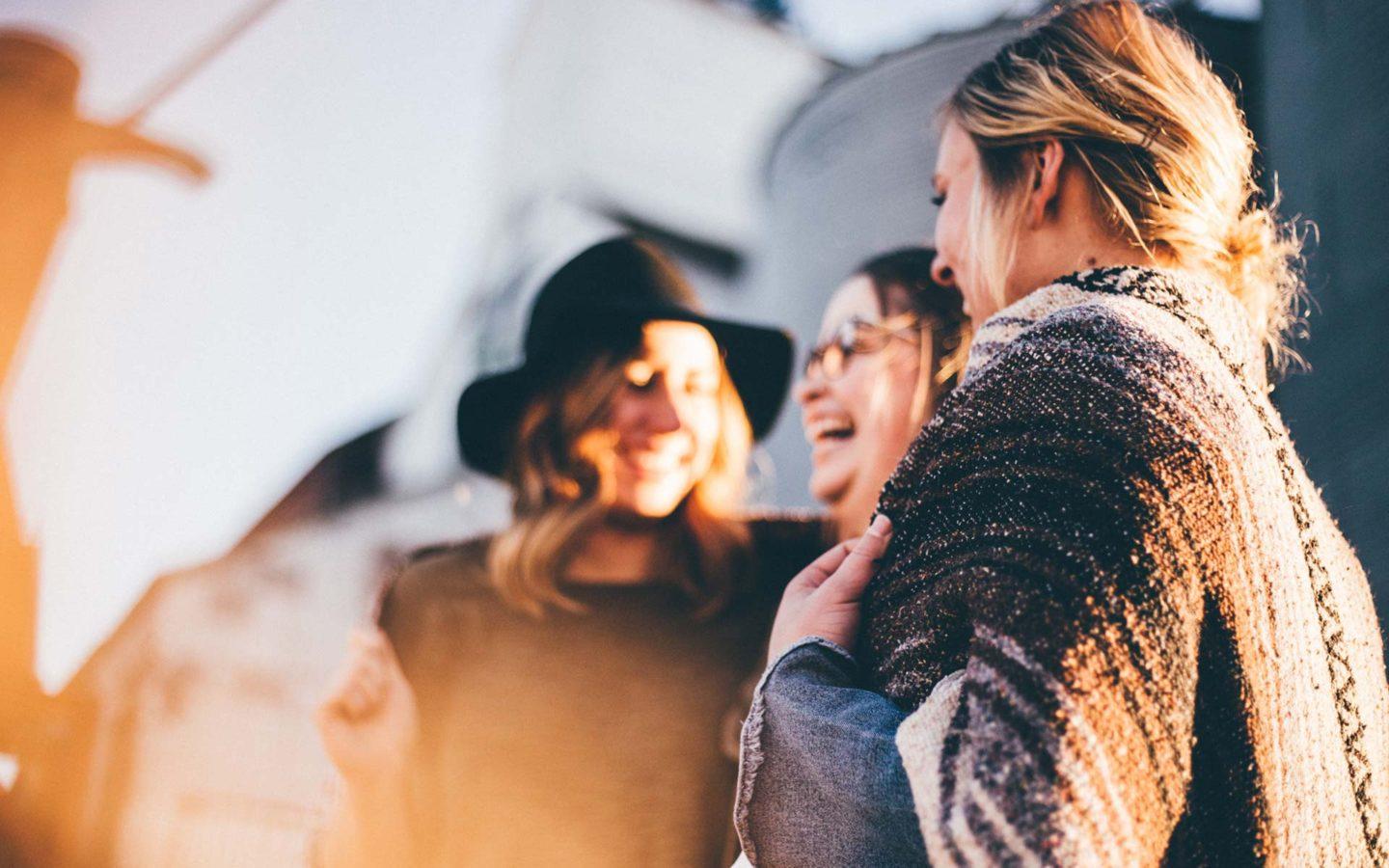 a close up photo of three women standing arm in arm laughing