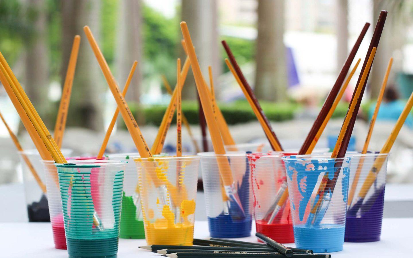 paint brushes sitting in cups filled with different paint colours